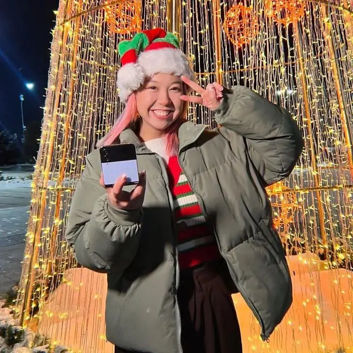 Alina holding a Samsung Z flip 4 while standing infront of a LED Christmas tree.